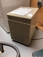 Front view of beige Damby Compact 30 dehumidifier with front vent and control knob. Manual and tags placed on top.