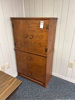 Front view of medium brown wooden dresser with two upper cabinet doors and three lower drawers with diamond-shaped wooden handles.