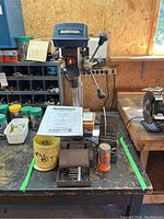 Mastercraft 10-inch drill press on workbench with manual and containers of assorted drill bits.