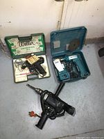 Photo showing Weller soldering kit, Makita blue cordless drill in case, and black Makita corded drill on floor
