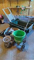 Overview of lot items including the garden wagon, seed spreader, bird bath, tote with gardening tools, and garden stakes on concrete floor in garage.