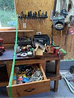 Overview of wooden workbench with screwdrivers on wall rack and various tools on bench including hand planes, pliers, mitre box, and measuring tapes. Drawer partially open with contents visible below.