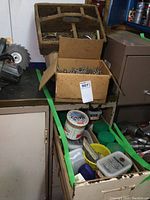 Wooden nail box with compartments filled with nails on top of a cabinet, cardboard box of nails in front, and drawer below with various containers and nails