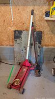 Two jacks side by side against garage wall, red hydraulic jack on left, black and red farm jack on right