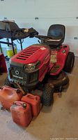 Front three-quarter view of red Troy-Bilt riding mower with three orange jerry cans placed in front