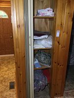 Wide view of the wooden linen closet shelf showing stacks of folded linens including bed sheets, towels, placemats, mats and wool blanket