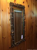 Full view of rectangular mirror with textured resin frame against wood wall.