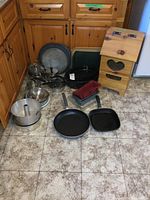 Photo of all cookware items along with the solid pine potato bin placed on tiled kitchen floor, showing assembled pots, pans, trays, and baking molds.