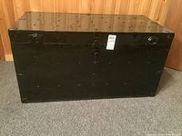 Front view of large black metal steamer trunk with lock and rivet detailing.