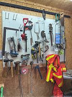 Wide view of pegboard showing a variety of hand tools and safety vests hanging on hooks.