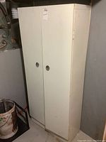 Front angle view of white metal storage cabinet with two doors and recessed handles, showing entire unit.