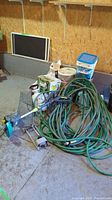 Wide view of lot items on concrete garage floor against plywood wall including trimmer, hoses, trap, buckets, and sprayers