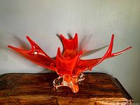 Frontal photo of blown glass centerpiece bowl showing organic abstract shape with multiple elongated spikes and a clear base on a wooden surface.