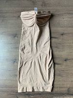 Flesh-toned, strapless body wrap shapewear laid flat on wood floor showing front side with bust detailing and smooth fabric body.