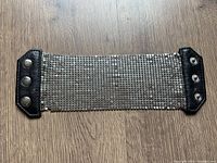Full view of wide silver mesh bracelet laid flat on wooden surface showing black leather ends and metal studs