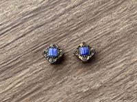 Photo of two square clip-on costume earrings with a blue center stone and decorative silver-tone metal around it, forming a diamond shape.