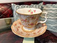 Side view of Royal Albert Bone China cup on matching saucer, showing beige and white floral design with pink rose accents and gold trim.