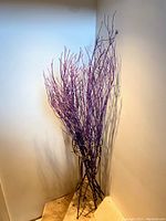 Full view of the decorative purple twigs arranged in the metal stand against a white wall.