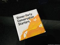 Front view of the game box with title Dinner Party Conversation Starters and yellow-orange splash design.