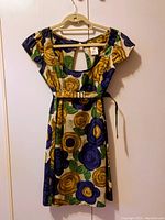 Full view of the floral dress hung on hanger showing front, short sleeves, floral pattern, and belt.