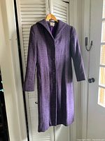 Front view of the long purple wool coat with hood and buttons hanging on hanger.