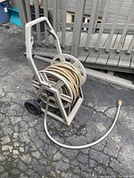 Full view of beige garden hose wrapped on a metal spinner reel with wheels and handle on cracked pavement.