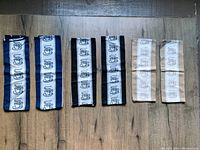 Seven hand towels laid out on a wooden floor, with coffee cup design down the center. Three have navy blue borders, two black borders, and two beige borders.