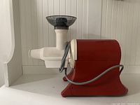 Photo of the electric centrifugal juicer showing red base, white juicing chamber and chute, and attached power cord