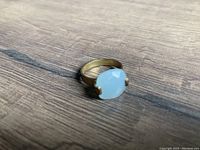 Photo showing gold-tone ring with white oval stone set on a wood surface.