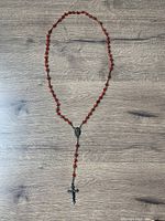 Full view of the rosary with red beads, Saint Theresa medallion, and metal crucifix on wood surface.
