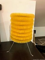 Small yellow brush table lamp off, showing stacked bristle rings and tripod legs