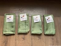 Four folded green napkins with woven checkered pattern