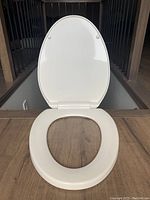Front view of white plastic toilet seat cover with lid open, showing overall condition and shape