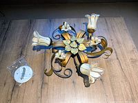Overhead view of one floral ceiling light fixture showing flower-shaped glass shades and gold and black metal scrollwork with leaf details for decorative lighting.
