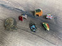 Seven vintage pins arranged on wood surface, depicting flags and themed motifs from US, UK, Italy, China and others.