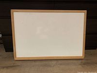 Front view of the rectangular whiteboard with a wooden frame, showing the clean white surface and minor scratch on the top left.