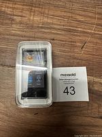 Front view of sealed Apple iPod Nano in plastic box showing home screen with app icons.