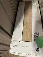 Boxes of American Olean ceramic floor tiles with hardwood texture. Close-up of box lettering and partial image of tile surface.