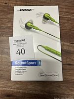 Front of sealed retail box showing lime green Bose SoundSport wired in-ear headphones with inline remote, branding, and compatibility icons