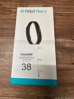 Front view of the Fitbit Flex 2 retail box showing product image and branding on wooden surface with auction card.