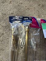 Photo showing brand new Levolor and Allison curtain rod sets in original plastic packaging lying on concrete surface.