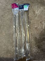 Three new expandable curtain rods packaged in plastic, placed on concrete background.