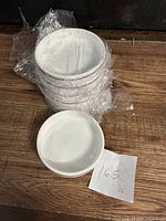 Stack of six white bone china bowls wrapped in protective plastic next to one bowl outside plastic on wooden surface.