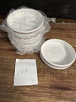 Five white bone china bowls stacked wrapped in plastic with one bowl outside the plastic. Each bowl has a thin purple-pink line around the rim. Photo includes handwritten note '168 x5'.