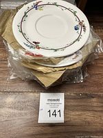 Stack of ten white saucers/plates with floral patterns visible on top, wrapped in plastic and brown paper for protection.
