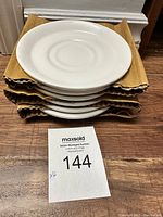 Stack of six white bone china saucers/plates with cardboard dividers between each plate, viewed from the top.