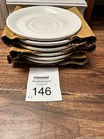 Stack of six white bone china saucers on brown protective padding.