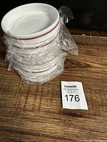Six stacked white bowls with a thin purple band around the rim wrapped in clear plastic showing brand new condition.