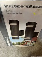 Box of set of 2 outdoor wall sconces showing brand name UberHaus and details of black finish and clear/frosted glass shades.