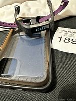 Black Fitbit fitness tracker on top of a clear iPhone case with a purple extra strap visible underneath